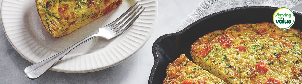 Cast iron skillet of zucchini and sun-dried tomato frittata with slices taken; servings shown to the side on side plates with fresh arugula salad.