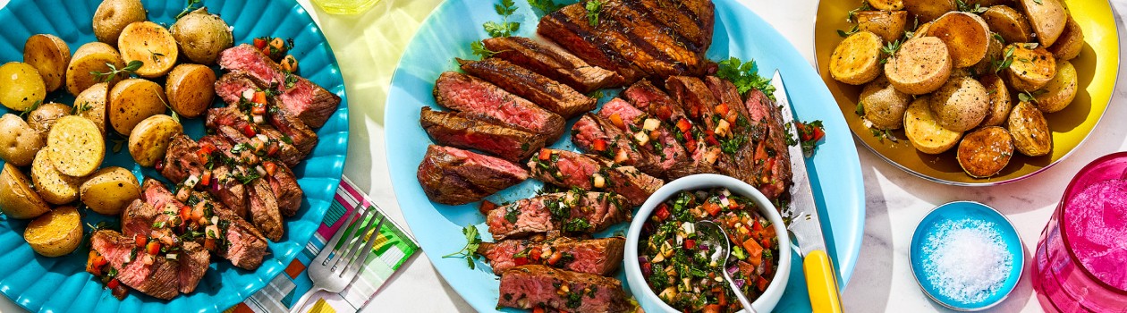 The plate in the centre has the tri tip steak sliced with the salsa on top and in a small bowl with two other plates surrounding it, one with potatoes and one with a combination of the sliced steak with salsa and more potatoes.