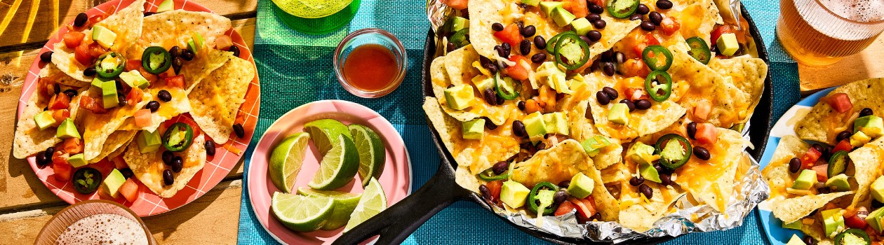 Overhead shot of campfire nachos in a skillet, topped with jalapenos, black beans, cheese, and avocado.