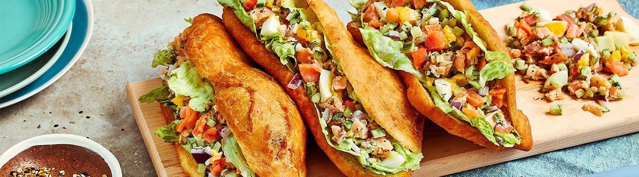 Three chopped smoked salmon bannock sandwiches on a wooden chopping block.