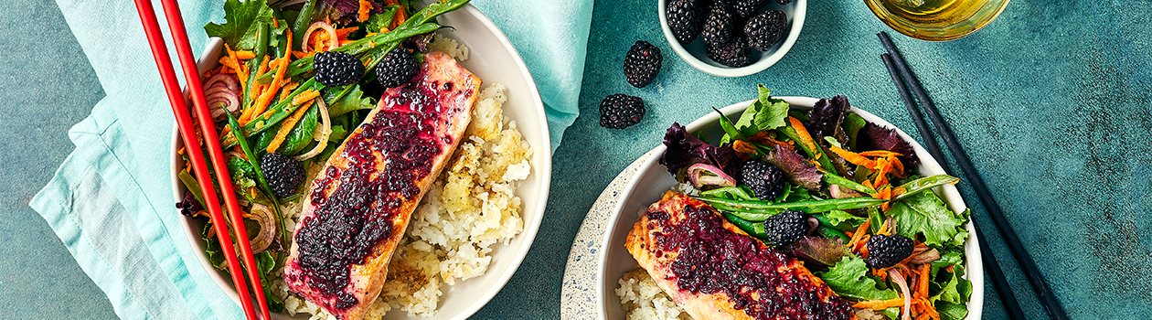 Two crispy rice bowls topped with vegetables, salmon filet and a blackberry glaze.