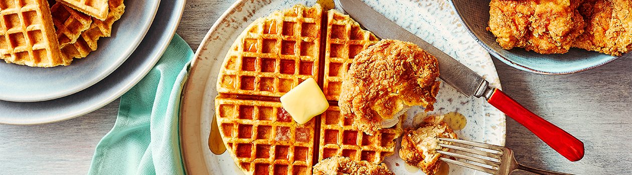 Fried chicken and bannock waffle on a white plate, with a plate of fried chicken and a plate of bannock waffles on the side.