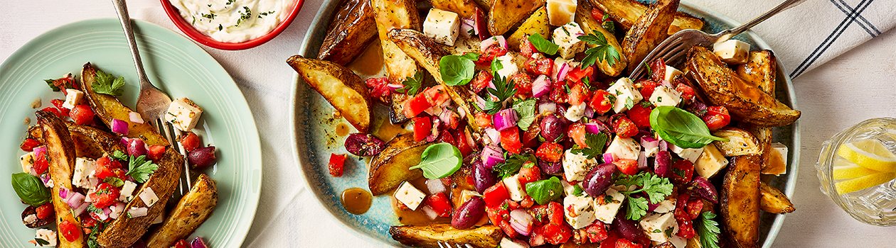Greek Poutine with two forks, a small plate off to the side, two drinks, and a bowl with tzatziki.