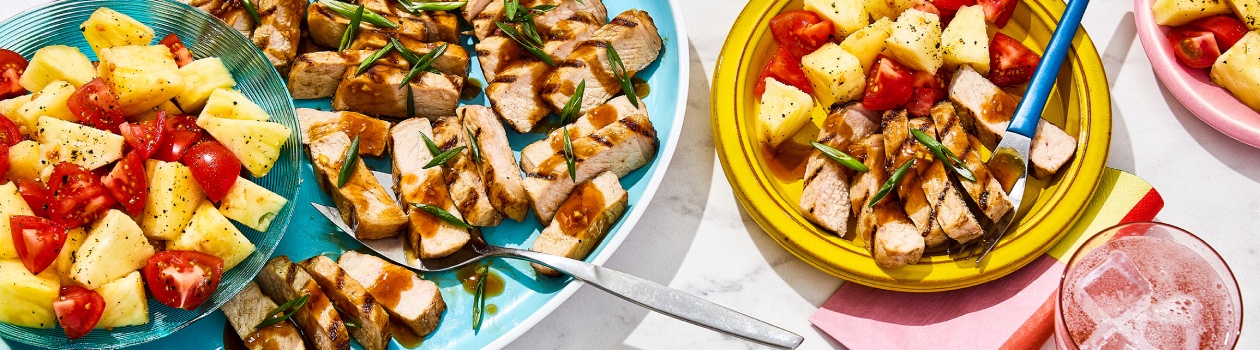 Grilled pork and pineapple salad on yellow plate with serving bowl to the left.