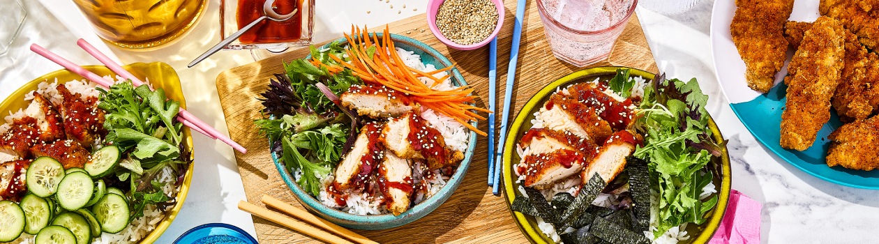 Korean chicken rice bowls topped with thinly sliced carrot, and sesame seeds.