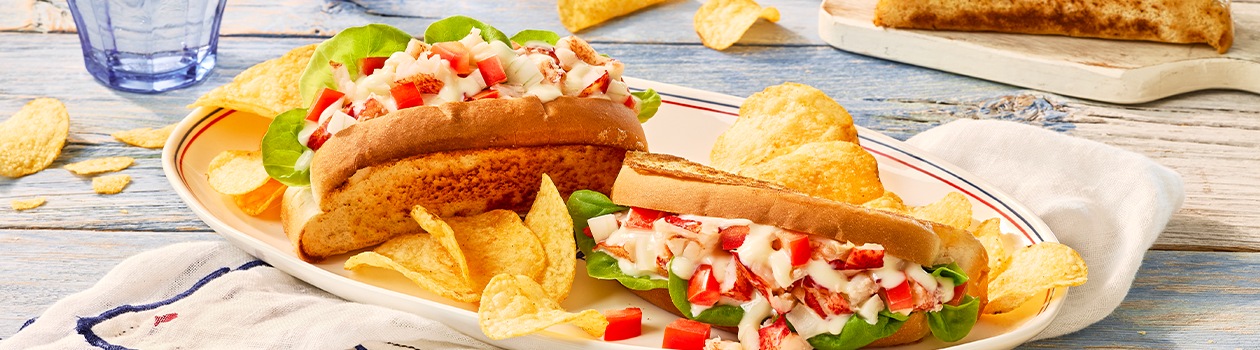 Two lobster rolls on a plate topped with Donair sauce with a side of chips