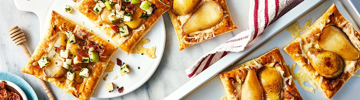 Three pear puff pastry tartlets on a plate, with two off to the side on a baking sheet.
