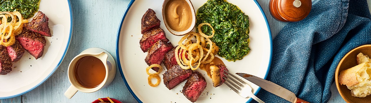 Sliced steak on white plate with side of creamed spinach
