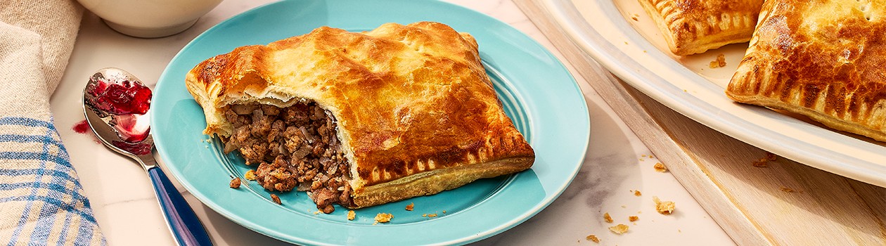 Tourtiere hand pie on a blue plate with a platter beside it.